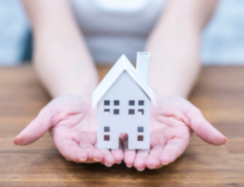 Person holding a small model house in their cupped hands, symbolizing home ownership or mortgage concept.